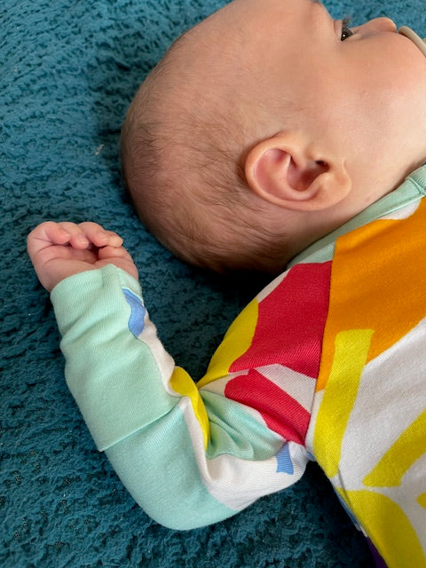 close up of baby wearing multi coloured long sleeve baby onesie with fold over hand 