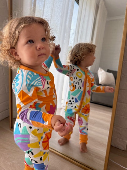 baby in mirror showing face and back of multi coloured long sleeve baby onesie with fold over hand and foot cuffs in unisex design