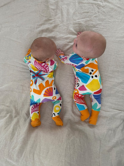 multi coloured long sleeve baby onesie with fold over hand and foot cuffs in unisex design. 2 baby models showing back of print