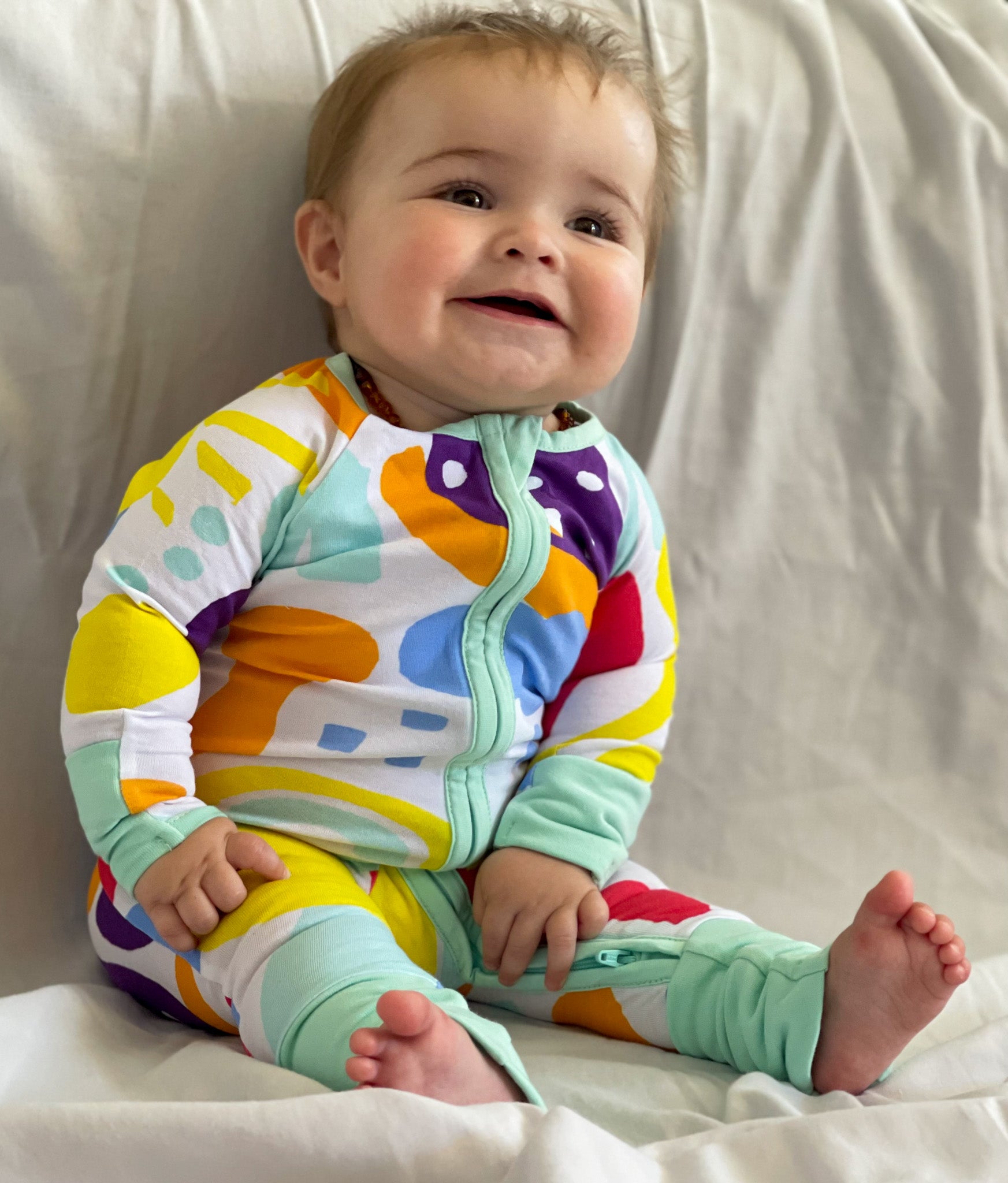 Baby wearing multi coloured long sleeve onesie with fold over hand and foot cuffs